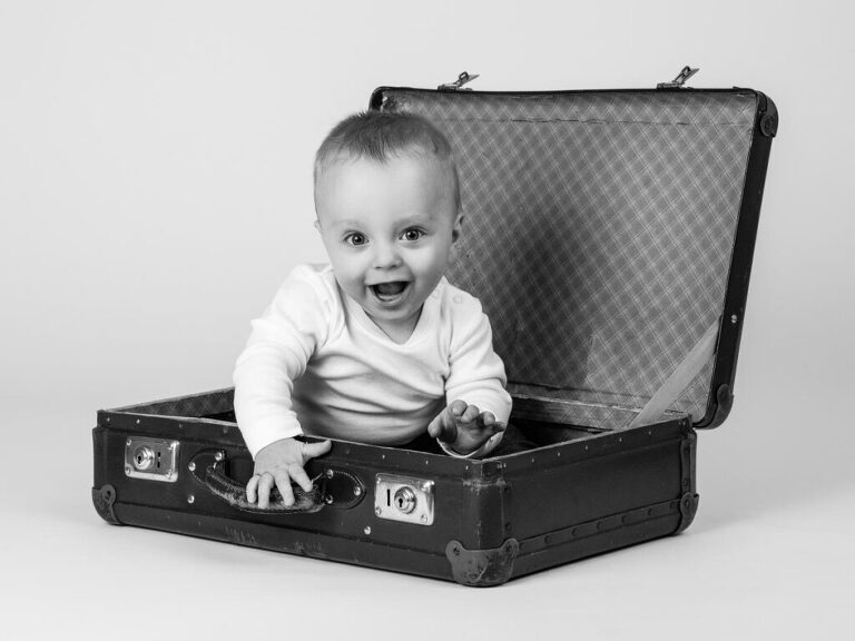 Svartvit bild av skrattande liten tandlös pojke som sitter i en resväska i Studio Lea