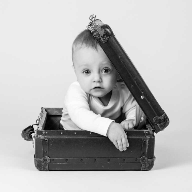 Svartvit bild av allvarlig liten pojke som sitter i en resväska i Studio Lea