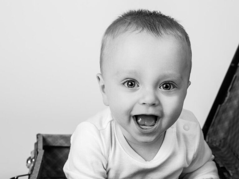 Närbild av glad liten tandlös pojke som sitter i en resväska i Studio Lea